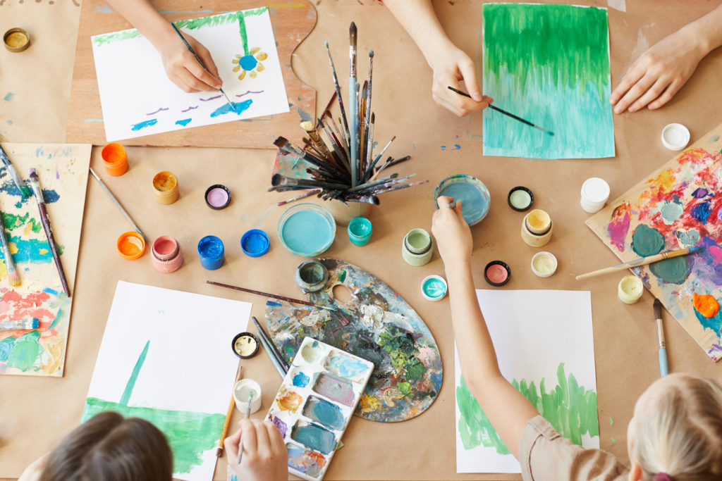 birds-eye view of a table of art supplies and several children working on projects around it